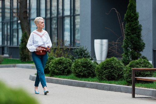 matured Female wearing white shirt and blue jeans while taking stroll past lush garden on both sides